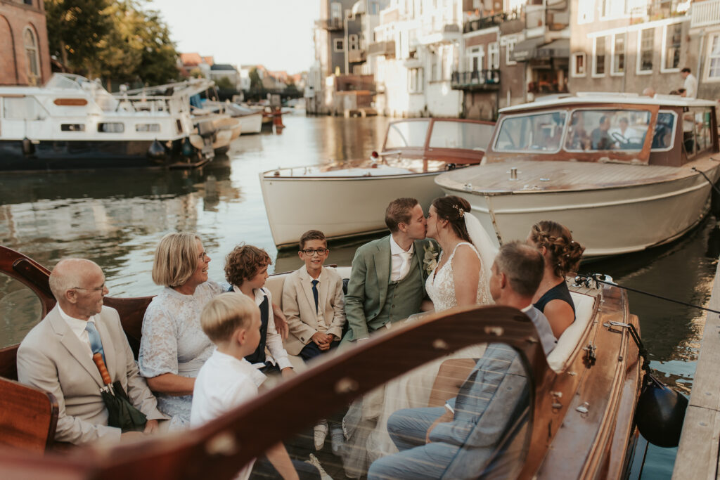 Zoenend bruidspaar, trouwen met boot in Dordrecht, zittend in boot met gasten